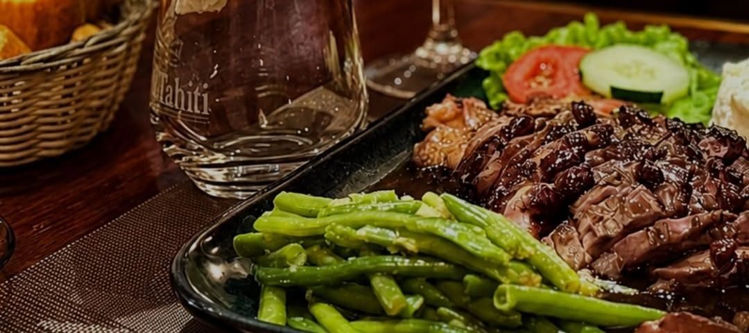 Magret de canard tranché, haricots verts et verre de vin rouge sur une table du Manava Café